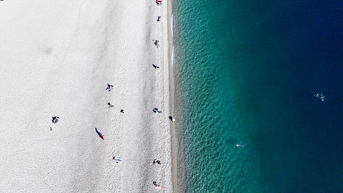 Çevresindeki dağların zirvesi karla kaplı Antalya'da güneşli havayı fırsat bilenler denize girdi....