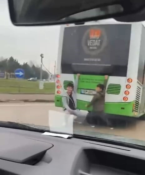 BURSA'DA OTOBÜSÜN ARKASINA TUTUNARAK AYAKLARINI YERE SÜRÜYEN 10-15 YAŞLARINDAKİ 2 ÇOCUK, TRAFİKTE...
